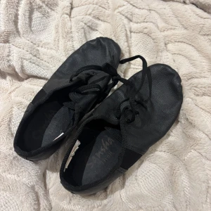 Svarta balettskor från Sansha - Säljer ett par svarta balettskor från Sansha. Skorna har snörning och är tillverkade i ett mjukt material som ger bra passform och flexibilitet. Perfekta för dans och träning.