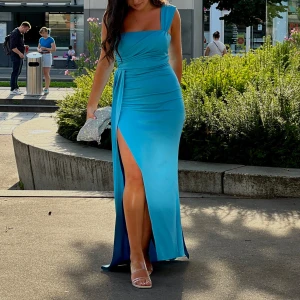 Blå fest klänning med slits - Elegant blå långklänning (enaxlad). en slits på sidan. Perfekt för en fest/som bröllops gäst. Klänningen har en draperad detalj vid midjan som ger en extra touch av stil. Klänningen är i ett väldigt bra skick! Storlek S 