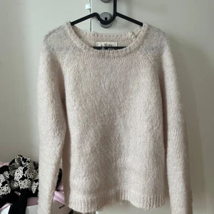 Vit stickad tröja - Mysig beige stickad tröja. Perfekt för kyliga dagar med sin mjuka och fluffiga textur. Tröjan har en rund halsringning och långa ärmar.