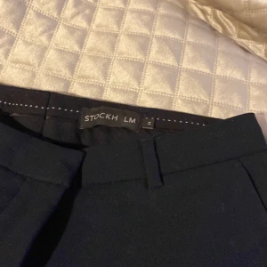 Svarta kostymbyxor från Stockh LM - Snygga svarta kostymbyxor från Stockh LM med en stilren design. Byxorna har en diskret ringdetalj vid midjan och är perfekta för en elegant look. De är tillverkade i ett bekvämt material som ger en bra passform.