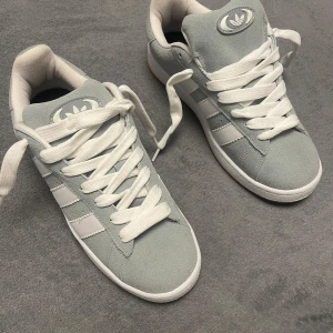 Grå sneakers från Adidas - Snygga grå sneakers från Adidas med klassiska vita ränder och logga på hälen. Skorna har en stilren design med snörning och en bekväm sula i gummi. Perfekta för en avslappnad stil. Skriv om du är intresserad dem är också helt NYA