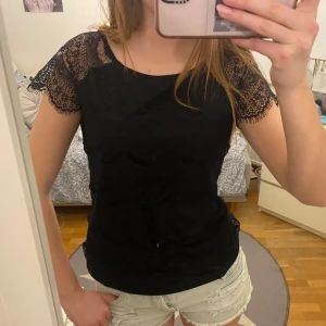 Svart spetsblus från KappAhl - Säljer en elegant svart spetsblus från KappAhl i storlek M. Blusen har korta spetsärmar och ett vackert mönster som ger en stilren look. Perfekt för att klä upp en outfit! 🌟