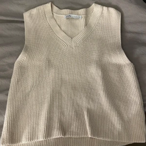 Beige stickad väst från Zara - Säljer en stilren beige stickad väst från Zara. Västen har en v-ringad design och är perfekt för lager-på-lager-stil. Den ribbade strukturen ger en snygg och modern look.💞