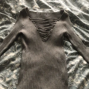 Grå ribbad tröja med snörning - Snygg grå ribbad tröja med lång ärm och unik snörning framtill. Perfekt för en stilren look.