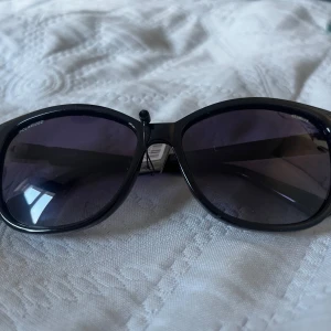 Svarta solglasögon från Bliz - Snygga svarta solglasögon från bliz med en klassisk design. De har en elegant svart båge med subtila gulddetaljer vid gångjärnen. Perfekta för att ge en stilren touch till din look.