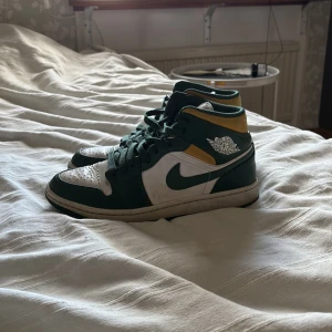 Nike Air Jordans i grönt och vitt - Snygga Nike Air Jordans i grönt och vitt med gula detaljer. Skorna har klassisk snörning och en hög design som ger bra stöd. Perfekta för dig som vill ha en stilren och sportig look. Det är mid