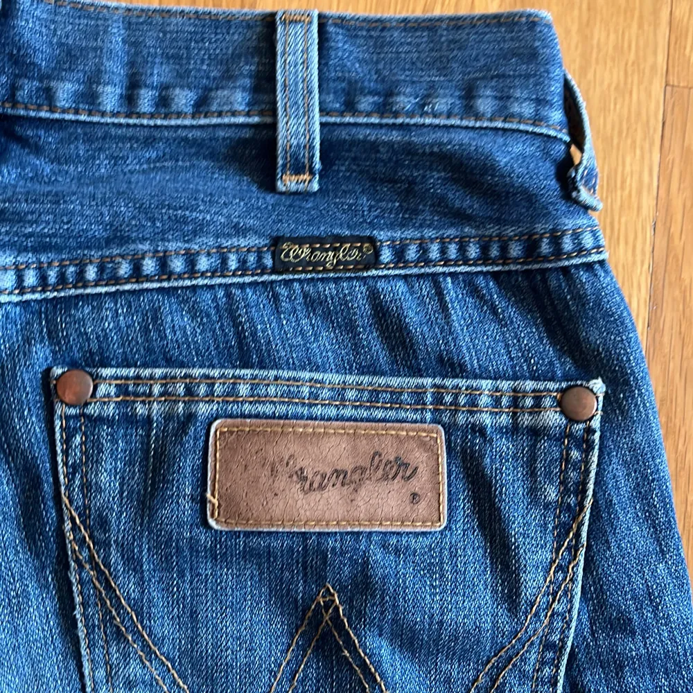 Säljer ett par klassiska blå jeans från Wrangler. De har en bootcut-stil och är tillverkade i slitstarkt denim. Jeansens baksida har de ikoniska Wrangler-detaljerna med lädermärke och kontrastsömmar.. Farkut & Housut.