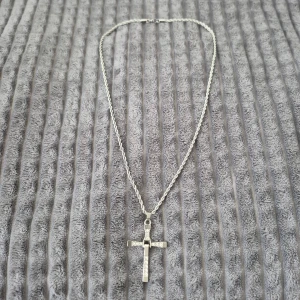 Stol silver halsband med korshänge - Snyggt stol silver halsband med ett korshänge dekorerat med glittrande stenar. Kedjan är tvinnad och har ett enkelt lås. Perfekt för att ge en stilren touch till din outfit.