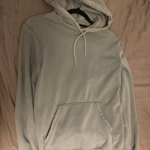 Grå/ grön hoodie från H&M - Säljer en stilren grå hoodie från H&M i storlek XS. Den har en avslappnad passform med en praktisk magficka och justerbar huva med dragsko. Perfekt för en bekväm och avslappnad stil.