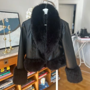 Svart skinnjacka med pälsdetaljer från BikBok - Snygg svart skinnjacka från BikBok med mjuka pälsdetaljer på krage, ärmslut och nederkant. Jackan har en croppad passform och är perfekt för att ge en lyxig touch till din outfit. Tillverkad i polyuretan och polyester.