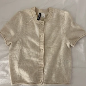 Beige kortärmad kofta från H&M Divided - Säljer en stilren beige kortärmad kofta från H&M Divided. Koftan har knappar framtill. Ändast testad och var för liten. Skulle vara perfekt för att ha flera lager, ny kostar den 200kr.