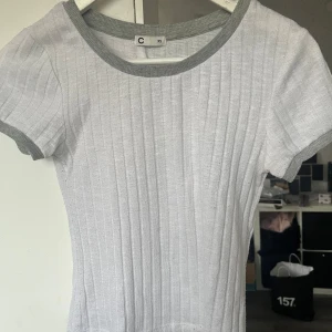 Vit ribbad topp med grå detaljer - Säljer en vit ribbad topp med grå kanter vid hals och ärmslut. Toppen har korta ärmar och en rund halsringning. Perfekt för en avslappnad stil. 🖤