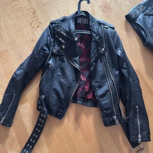 Svart skinnjacka från Jofama - Snygg svart skinnjacka från Jofama med coola detaljer som dragkedjor och bälte. Insidan har ett rött och svart blommigt mönster. Storlek 40 men funkar för en mindre person med 