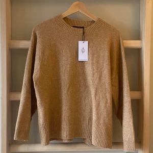 Beigebrun stickad tröja - Beigebrun stickad tröja med prislappen kvar. Tröjan har en rund halsringning och ribbade detaljer vid ärmslut och nederkant, och ger en arketkänsla men är från stradivarius. Perfekt för våren!