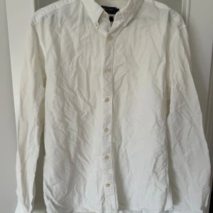 Vit skjorta från East West - Säljer en klassisk vit button-down skjorta från East West i storlek L. Skjortan har långa ärmar och knappar framtill. Perfekt för en stilren look.