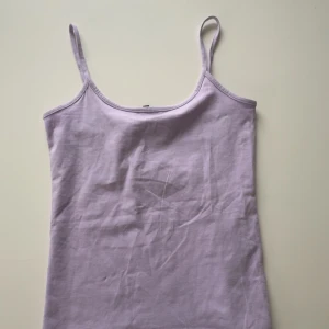 Ljuslila linnetopp - Säljer en ljuslila linnetopp med smala axelband. Perfekt för varma dagar och kan enkelt matchas med olika outfits. Toppen är i ett mjukt och bekvämt material. Har inte justerbara band. Aldrig använd 