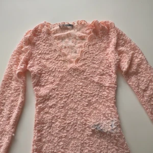 Rosa spetsblus från Gina Tricot - Säljer en söt rosa spetsblus från Gina Tricot i storlek XS. Blusen har en v-ringad design och långa ärmar, perfekt för en romantisk look. Den är helt i spets vilket ger en elegant touch. Perfekt för att piffa upp garderoben!