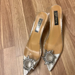 Transparenta pumps från Shein - Snygga transparenta pumps från Shein med spetsig tå och dekorativa pärlor framtill. Skorna har en elegant klack och en stilren design i silver och transparent material.