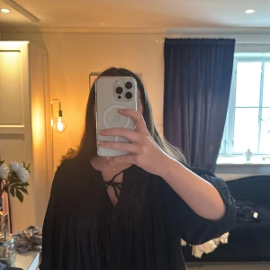 Svart blus från Gina Tricot - Säljer en svart blus från Gina Tricot med knytning vid halsen och knappar framtill. Blusen har långa ärmar och fina veckade detaljer på axlarna. Perfekt för en stilren look. I storlek L. 