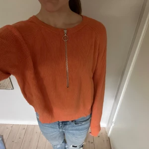 Orange stickad tröja med dragkedja - Snygg orange stickad tröja med lång ärm och cool silverfärgad dragkedja framtill. Perfekt färg och modell till hösten. Materialet är mjukt och ribbat.