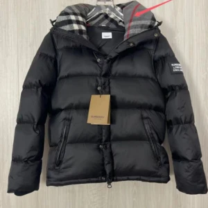 Svart pufferjacka från Burberry - Svart pufferjacka från Burberry med klassiskt rutigt foder i huvan och snygga detaljer. Jackan har dragkedja och knappar framtill, samt två praktiska fickor med dragkedja. Perfekt för dig som vill ha en stilren och varm jacka med exklusiv känsla.