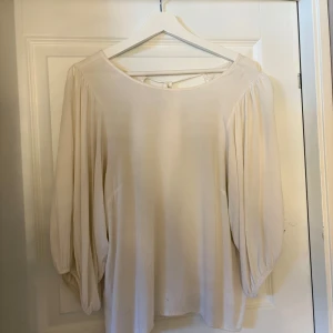 Beige blus med knytning i ryggen - Luftig beige blus med rund halsringning och knytning i ryggen.