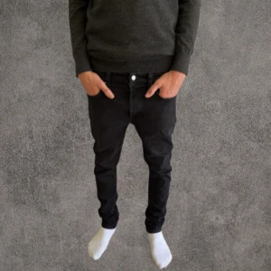 Svarta slim jeans från Nudie Jeans - Svarta jeans från Nudie Jeans med klassisk femficksdesign och snygga detaljer på bakfickan. Modellen är slim fit med smal passform hela vägen ner och har en stilren look. Jeansen är gjorda i stretchig bomull för extra komfort och har svarta sömmar och knappstängning.