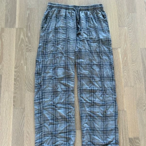 Grå-rutiga mjukisbyxor från 157 - Mysiga blå mjukisbyxor från 157 med rutigt mönster och dragsko i midjan. Byxorna har avslappnad passform och är perfekta för chill dagar hemma. Tillverkade i mjukt bomullstyg och har elastisk midja för extra komfort.