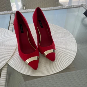 Röda pumps med gulddetalj Zara - Snygga röda pumps från Zara Basic Collection i storlek 38. Skorna har spetsig tå och guldfärgad metall-detalj framtill, samt klack med guldfärgad kant. Yttermaterialet är mocka och klacken är smal och elegant. Perfekt för dig som vill sticka ut med färg och stil.