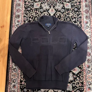 Mörkblå Polo Ralph Lauren half zip tröja - Snygg mörkblå tröja från Polo Ralph Lauren med stor broderad POLO-logga på bröstet. Modellen har half zip, hög krage och en stor magficka. Tillverkad i 100% bomull för skön känsla. Perfekt för dig som gillar klassisk streetwear med premiumkänsla.