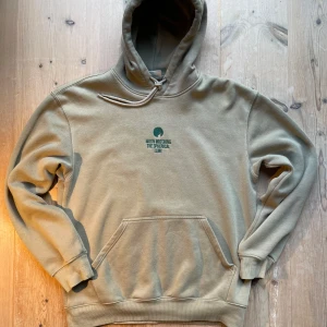 Grön hoodie från H&M med brodyr - Säljer en grön hoodie från H&M med avslappnad passform. Tröjan har huva med snörning, magficka och broderad text 'Moon Watching The Spherical Lune' i mörkare grönt på bröstet. Skriv vid intresse!