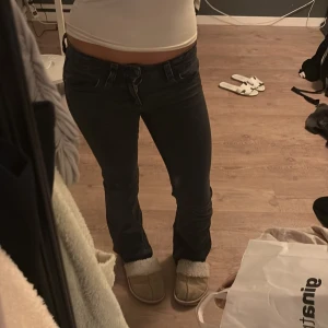 Svarta bootcut jeans låg midja - Säljer ett par svarta jeans med låg midja och bootcut-snitt. Snygg passform som sitter tajt över låren och släpper vid vaden. Klassisk femficksmodell (knapparna på baksidan är av men inget synligt) med dragkedja och knapp framtill. Perfekta till sneakers eller boots.