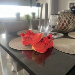 Asics novablast 5  - Säljer ett par riktigt snygga Asics sneakers i röd färg med svarta detaljer. Skorna har en sportig design med mesh-ovandel, snörning och en tjock, platt sula i rött och beige. Perfekta för dig som gillar att sticka ut och vill ha grym komfort till träningen.