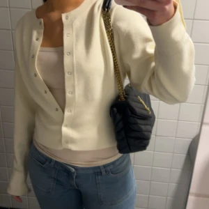 Krämvit kofta från Gina Tricot - Superfin krämvit kofta från Gina Tricot med rund hals och långa ärmar. Koftan har knappar hela vägen framtill och är lite croppad i modellen. Perfekt att slänga över en topp till jeans för en chill look. Materialet är mjukt och känns skönt mot huden.