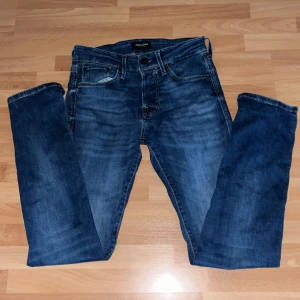 Blå jeans från Jack & Jones - Snygga blå jeans från Jack & Jones med klassisk femficksdesign och lätt tvättad look. Jeansen har rak passform och normal midja, vilket gör dem sköna och stilrena. Perfekta för dig som gillar en enkel och tidlös stil.