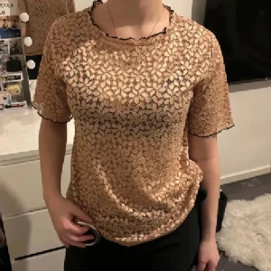 Beige spetsblus från Zara Trafaluc - Säljer en beige blus från Zara Trafaluc i storlek S. Blusen är gjord i spets med blommigt mönster och har svarta detaljer längs kanterna. Den är kortärmad och har en loose passform, perfekt för dig som gillar en chill och snygg stil.