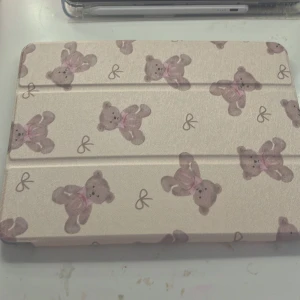 Ett iPad skal  - Söt ipad skal i beige med gulligt mönster av bruna nallar och små rosetter. Väskan har ett hårt skal med transparent baksida och vikbar framsida. Perfekt för dig som vill ha en unik och charmig look till din laptop eller surfplatta.