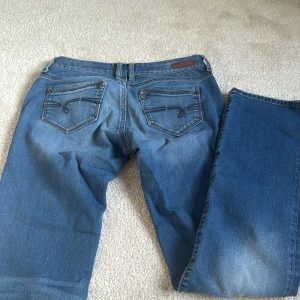 Blå jeans från Mavi Jeans Co. - Snygga blå jeans från Mavi Jeans Co. med klassisk femficksdesign och coola detaljer på bakfickorna. Jeansen har normal passform och raka ben, med slitningar och tvättade partier för en avslappnad look. Low waist. Materialet är robust denim med orange sömmar. Saknar knapp. Stolek 28/32. Pris går att diskutera💞