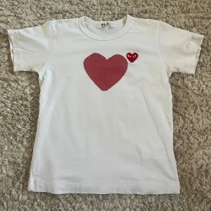 Vit t-shirt från comme des garcobs - Säljer en vit t-shirt från comme des garcobs med korta ärmar och rund hals. På bröstet finns ett stort rött hjärta och ett mindre hjärta med ögon, och på ryggen ett stort hjärta med ögon. T-shirten är gjord i mjuk bomull och är superskön! Nypris: 1300!  Inga defekter💞Tröjan är i barn L men passar bra för xs och s! Hör gärna av er om ni har frågor eller prisförslag!💞