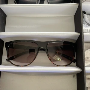 Svarta VonZipper solglasögon med guld Ny pris 1200 - Snygga solglasögon från VonZipper med svart och guld detaljer på skalmarna. Stora, fyrkantiga bågar i plast med tonade linser som går från mörkt till brunt nedtill. Perfekt för dig som vill sticka ut med en cool och modern look.