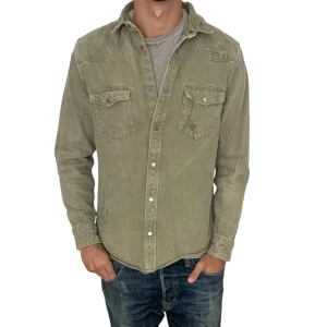 Olivgrön overshirt med slitningar  - Olivgrön overshirt i bomull med klassisk krage och två bröstfickor med lock och knapp. Långärmad modell med tryckknappar framtill och på fickorna. Perfekt att bära över en t-shirt för en avslappnad look.
