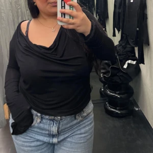 Svart långärmad omlottopp - Säljer en svart långärmad topp med omlott och draperad v-ringad halsringning. Snyggt flowy tyg som sitter skönt mot kroppen och ger en chill men ändå stilren vibe. Perfekt att matcha med jeans eller kjol för en cool look.