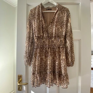 Jättesnygg leopardmönstrad kort klänning från Zara - Säljer en superfin kort klänning från Zara i storlek xs med leopardmönster i beige och bruna toner. Klänningen har v-ringning, smockad midja och volangdetaljer nertill. Långärmad och tillverkad i ett lätt, transparent syntetmaterial. Den är i bra skick, har en fin passform och är perfekt som bland annat strandklänning🌸Den är en perfekt längd med fina detaljer och är super skön. Skriv om funderingar, priset kan diskuteras och lämna gärna omdöme om köpt😊