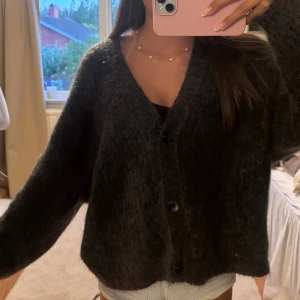 Mörkgrå oversized kofta med knappar - Säljer en supermysig mörkgrå kofta med oversized passform och stora knappar framtill. Koftan är stickad och har långa ärmar, perfekt att slänga på sig när det är lite kyligt ute. Passar dig som gillar en chill och avslappnad stil.