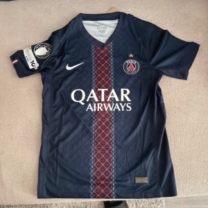 PSG Dembele #10 fotbollströja Nike - Snygg marinblå PSG fotbollströja med O. Dembélé och nummer 10 på ryggen. Tröjan har korta ärmar, V-ringning och detaljer i rött och vitt, samt Qatar Airways som sponsor på bröstet. Tillverkad i lätt och ventilerande material, perfekt för match eller träning.