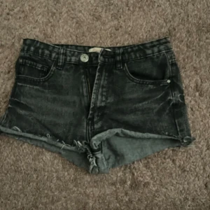 Svarta jeansshorts från Regular - Snygga svarta/mörkgråa jeansshorts från Regular. De har dragkedja och knapp framtill, bälteshällor och slitna detaljer för en cool vibe. Perfekta för sommaren och passar till allt. Kort modell med midwaist.