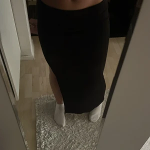 Svart långkjol med slits - Säljer en svart långkjol med slits på sidan. Kjolen har en tight passform och är enkel och stilren, perfekt för dig som gillar minimalistisk stil. Materialet känns mjukt och följsamt mot kroppen.