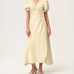 Adoore klänning - Säljer en ljusgul långklänning med små blommor, omlottmodell och puffiga kortärmar. Klänningen har v-ringning och knyt i midjan för en snygg siluett. Perfekt för dig som gillar romantisk och feminin stil. Använt 1 gång 