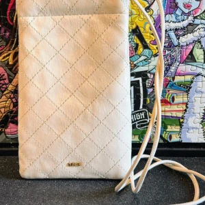 Mobilväska från Mango - Snyggt benvitt mobilfodral med dekorativa sömmar, en guldfärgad Mango logga och ett långt justerbart handtag. Tryckknappsstängning. Innerfoder. Det är helt nytt och oanvänt i jättebra skick! 11.0x18.0x2.0 cm (Längd x Höjd x Bredd). Tillverkad i polyuretan med polyester innerfoder 