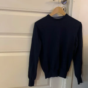 Mörkblå stickad tröja med armbågslappar från Stenströms - Snygg mörkblå stickad tröja från Stenströms. Tröjan har rund hals och långa ärmar med ljusare blå armbågslappar som ger en cool detalj. Perfekt för dig som gillar klassisk stil med en twist. Ribbstickade muddar vid ärmslut och nederkant. Passar S